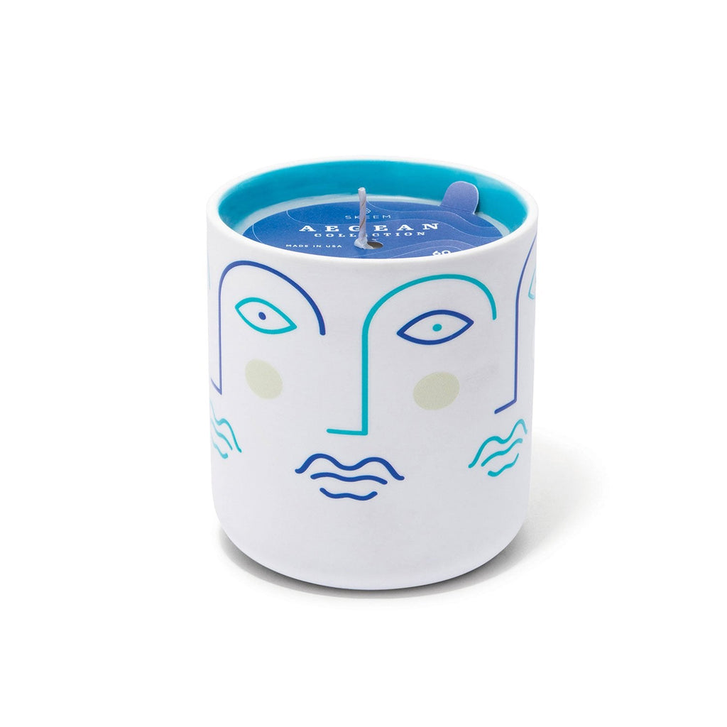 The Skeem Hellenes Faces Aegean Candle, Fig, is a white jar with minimalist abstract blue and green facial designs for a Mediterranean escape. Filled with fig-scented blue wax, it has a single wick and artistic eyes and lips. Decorative paper adorns the top for an exquisite finish.