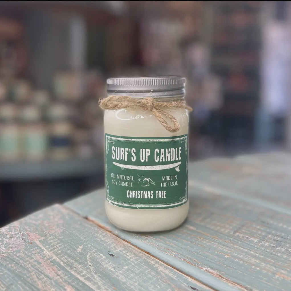 A Surfs Up Candles Surf’s Up - Christmas Tree Mason Jar Candle sits elegantly on a distressed wooden surface. Made from all-natural soy wax, this eco-friendly glass jar with a metal lid and twine enhances any cozy store setting or room decor.