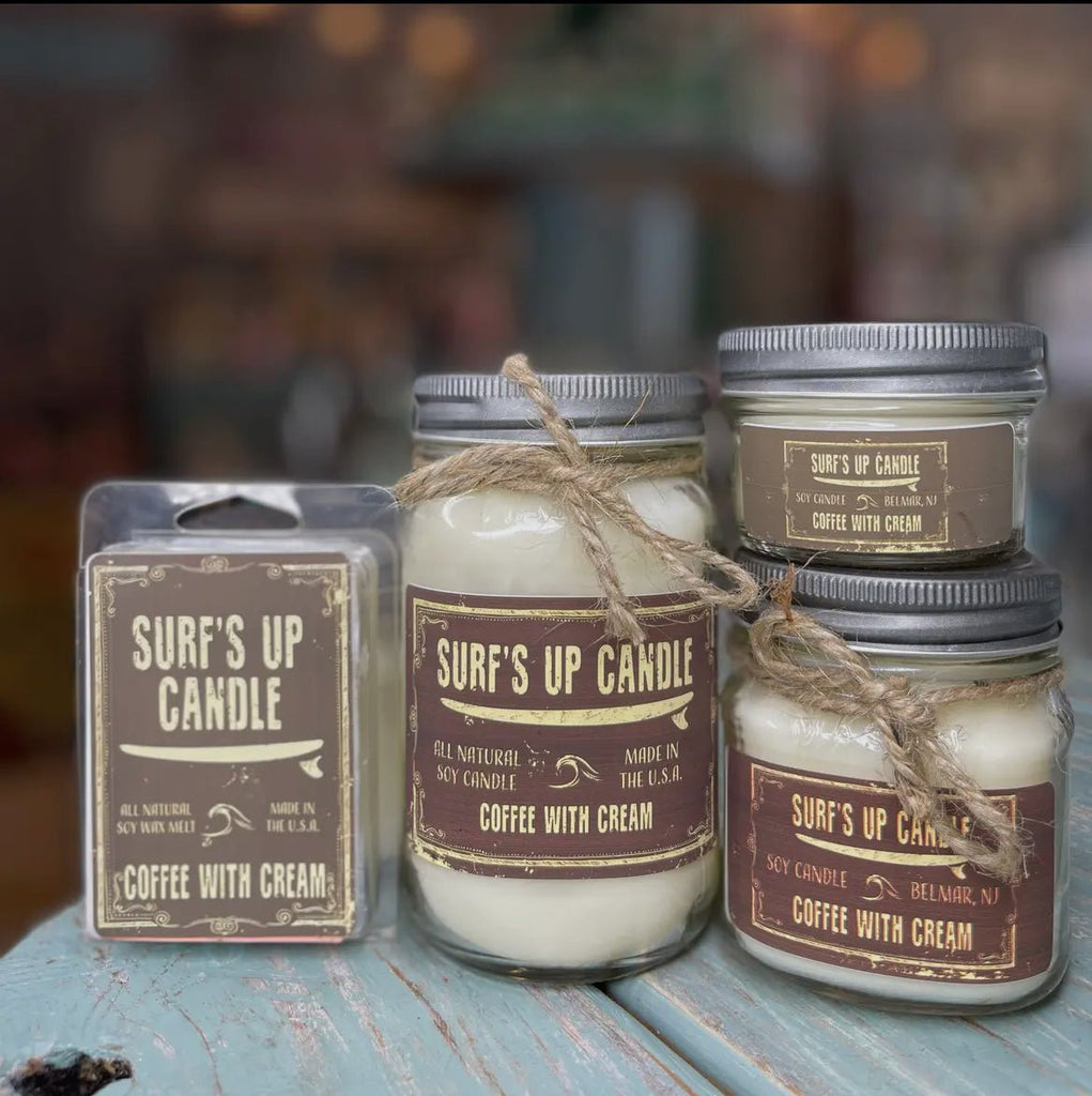 Four Surf’s Up candles in the Coffee with Cream scent by Surfs Up Candles include a large reusable mason jar with twine, a smaller glass jar, and two wax melt packages made from natural soy wax, all displayed on a rustic teal surface.