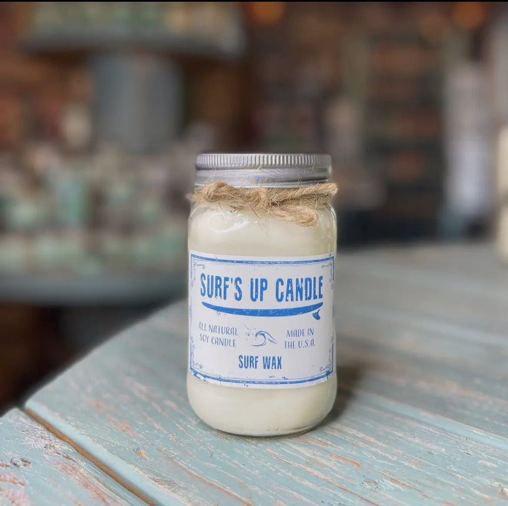 A Surf’s Up - Surf Wax Mason Jar Candle from Surfs Up Candles rests on a weathered turquoise table. Its an all-natural soy wax candle, made in the USA, with a surf wax scent. The softly blurred background adds a dreamy touch.