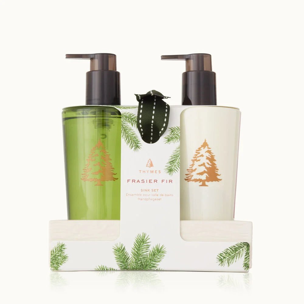 The Thymes - Frasier Fir Sink Set includes two pump bottles, Hand Wash and Hand Lotion, in green and white with fir tree designs and comes in a decorative holder boasting green fir illustrations.