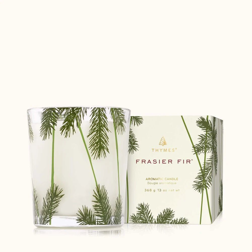 The Thymes - Frasier Fir 13oz Pine Needle Poured Candle features pine needle designs and comes with a matching box, both reflecting a botanical theme on a light background.