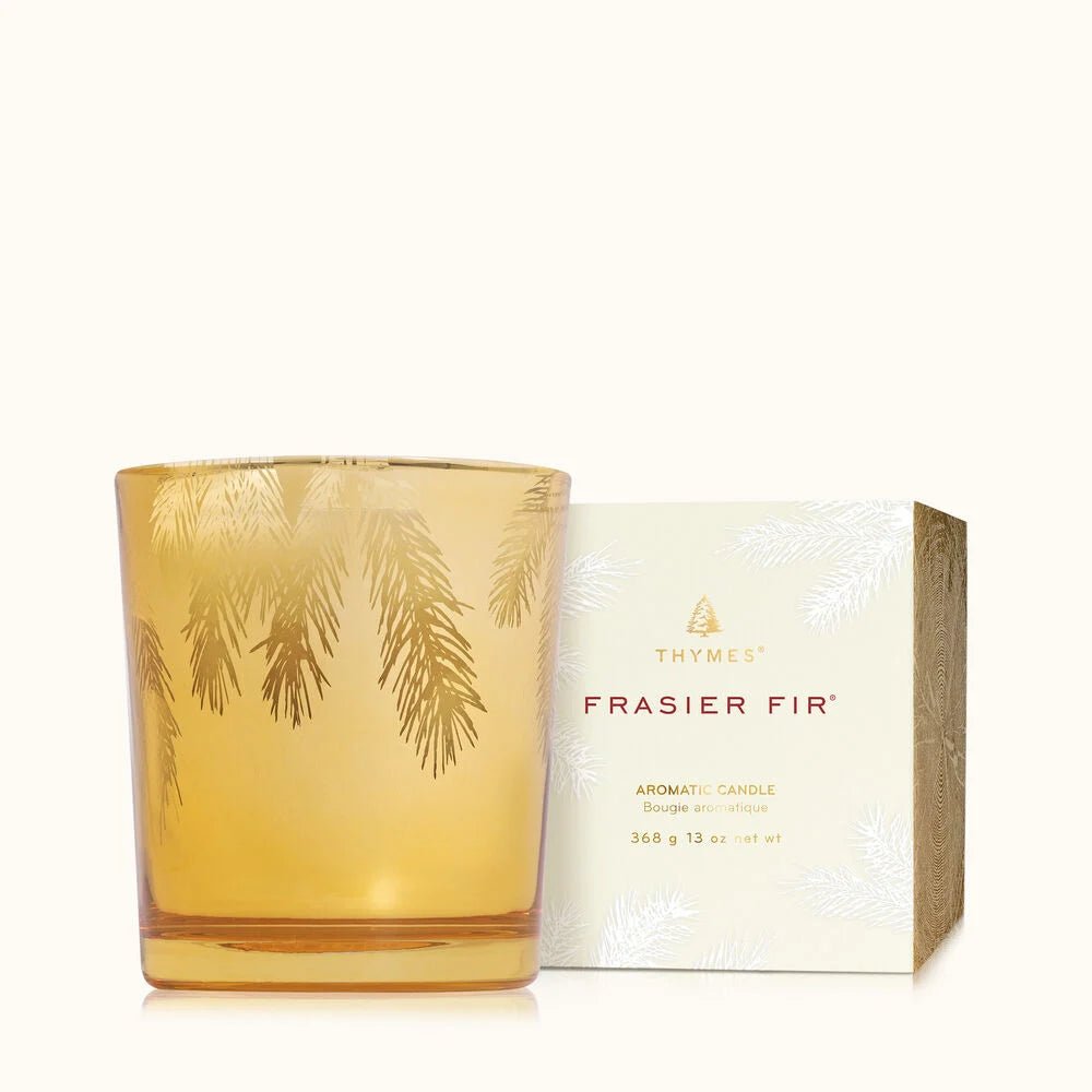The Thymes Frasier Fir Gilded 13 oz Poured Candle features elegant pine needle designs and comes with a matching box, both accented with pine branch patterns for a festive touch.