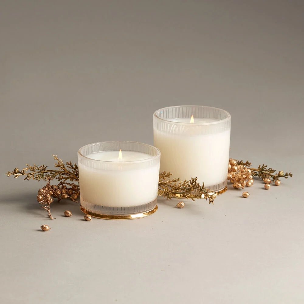 Two Thymes Frasier Fir Gilded Frosted Wood Grain candles are lit in frosted glass holders. Their Siberian Fir scent and gold accents add a serene, festive touch against the neutral background.