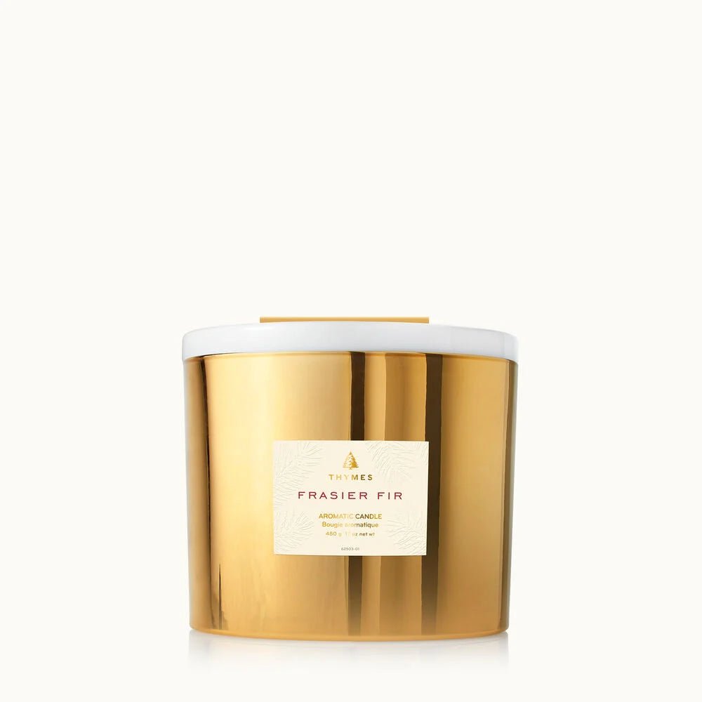 A gold, reflective Thymes Frasier Fir Gold 3-Wick Candle with a white lid rests against a simple background, filling any space with the signature mountain fresh scent.