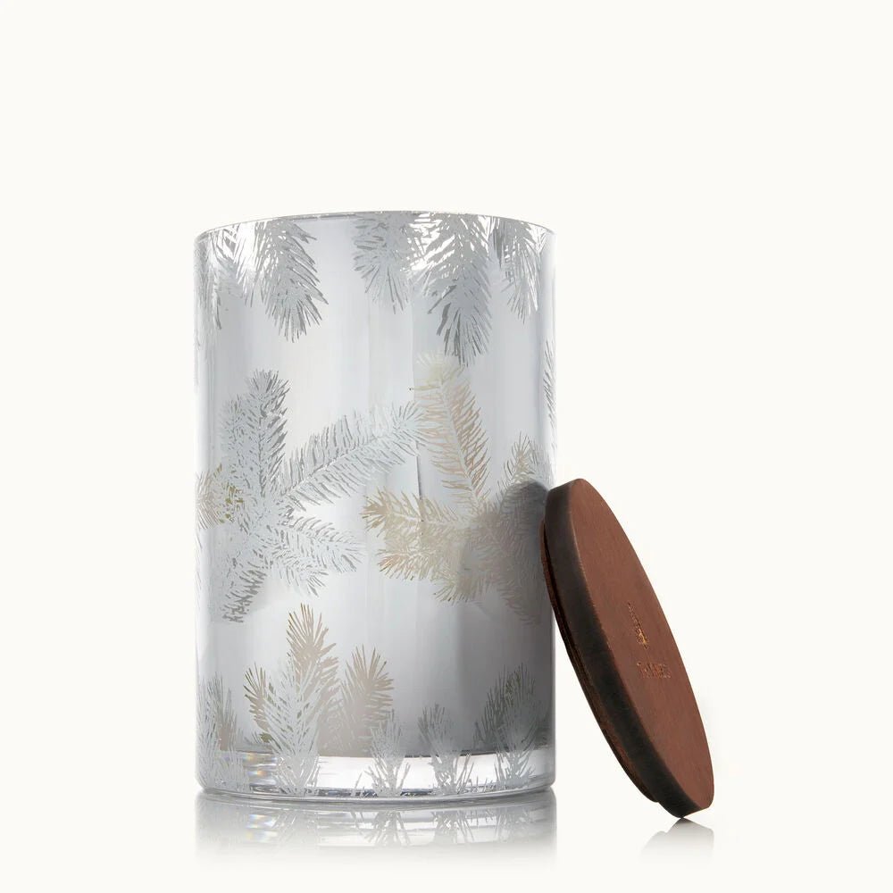 The Thymes - Frasier Fir Statement Medium Luminary Candle features a clear glass jar with frosted pine branch designs and a round brown wooden lid, evoking the crisp scent of Siberian Fir.