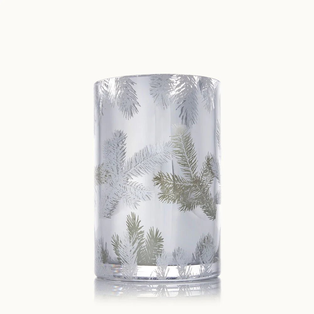 The Thymes Frasier Fir Statement Medium Luminary Candle is a clear glass holder adorned with frosted and metallic pine branch designs, shown upright against a plain white background.