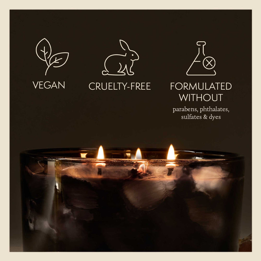 The Thymes Noir Woods 3-Wick Poured Candle in a dark glass jar sits below icons and text reading: Vegan, Cruelty-Free, and made without parabens, phthalates, sulfates or dyes, infusing the air with a luxurious, smoky wood aroma.