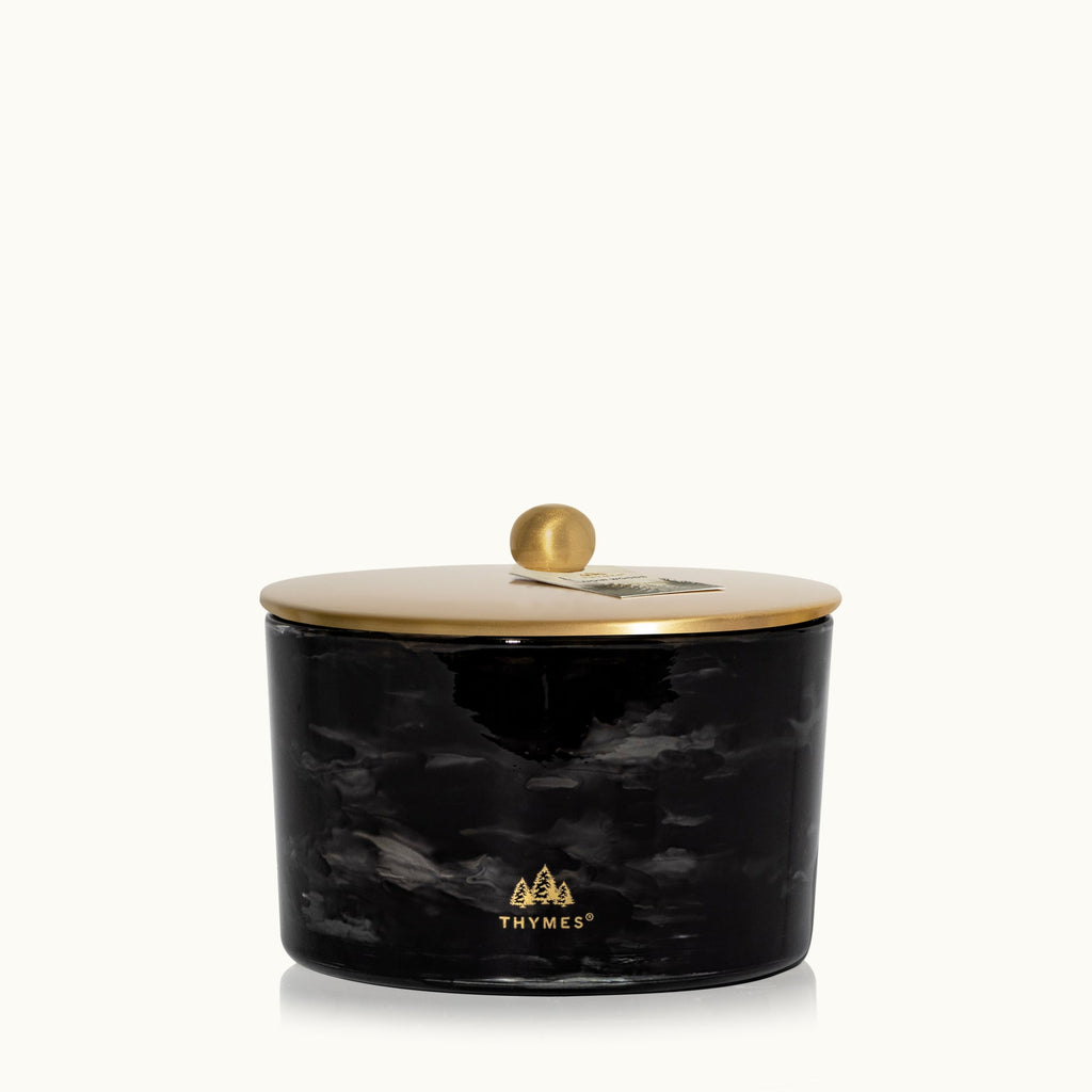 The Thymes Noir Woods 3-Wick Poured Candle features a black marbled glass jar with a gold lid, adorned with the Thymes logo and tree icons, and fills your space with a refined smoky wood scent.
