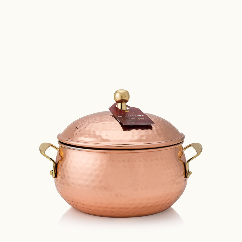 The Thymes Shimmered Cider Copper Pot 3-Wick 18oz Aromatic Candle features a hammered copper pot with lid, gold handles and knob, plus a maroon tag on top, all set against a plain light background.