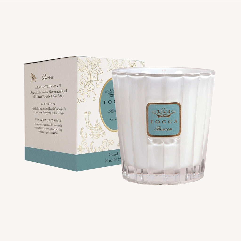 The Tocca - Bianca 10oz Candle is luxuriously packaged in a white, textured glass holder and comes with a matching box featuring elegant blue and cream designs to enhance its sophisticated appeal.