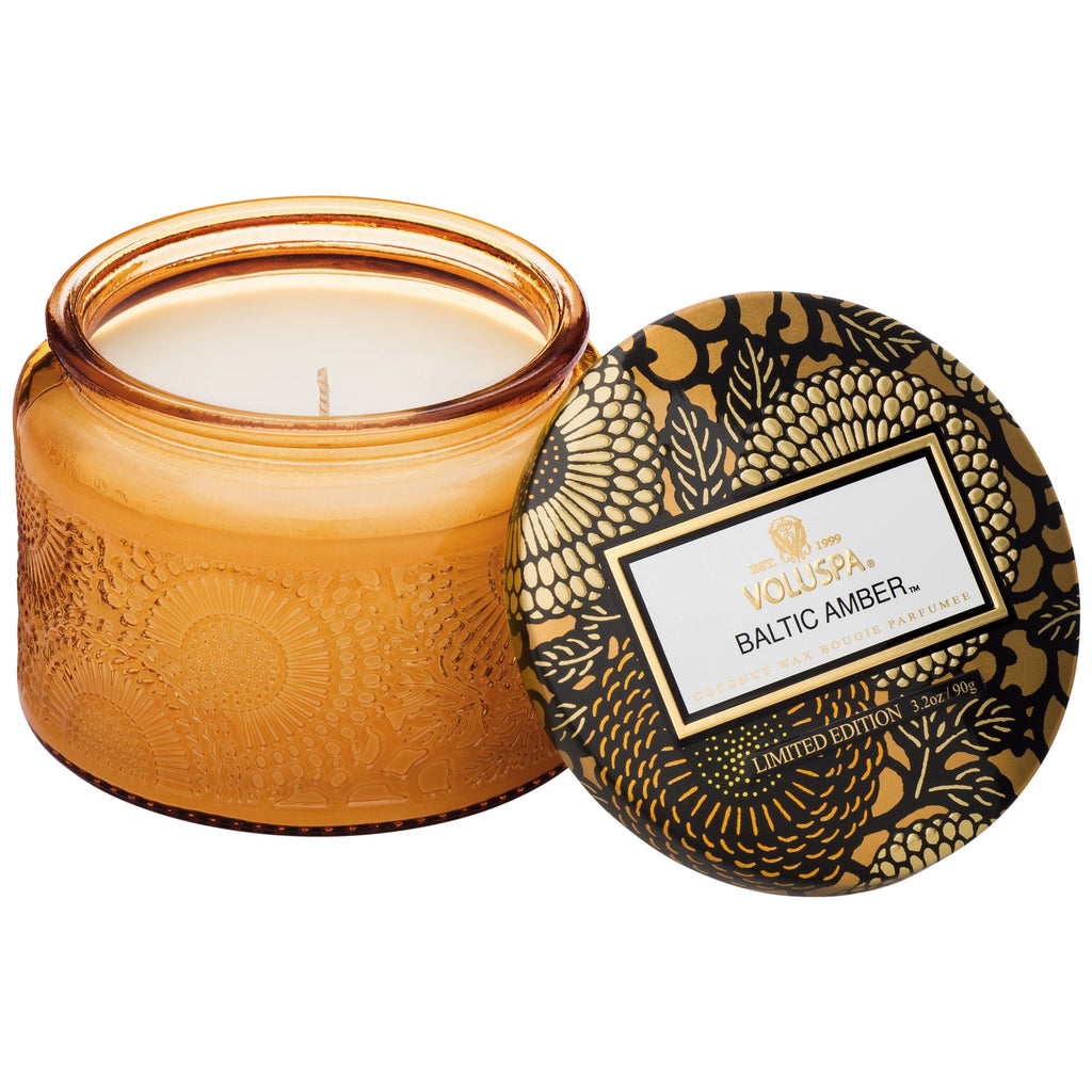 The Voluspa Baltic Amber Petite 3.2oz candle, part of a limited edition collection, features a coconut wax blend in an amber glass jar with intricate patterns and a gold-and-black floral lid.