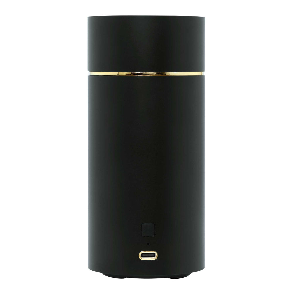 The Voluspa Black Ultrasonic Fragrance Oil Diffuser Device is sleek and cylindrical with a smooth black finish. It features a USB-C charging port at the base and a gold accent ring near the top, enhancing its modern, minimalist cordless design.