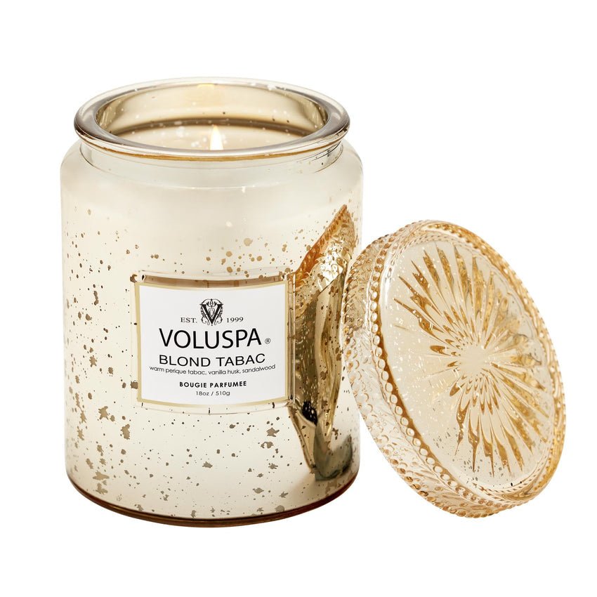 The Voluspa Blond Tabac Large Jar 18oz Candle in a gold-speckled glass jar has a Perique tabac aroma, with its lid stylishly leaning against the jar. The neutral-hued coconut wax blend offers an elegant and luxurious look.