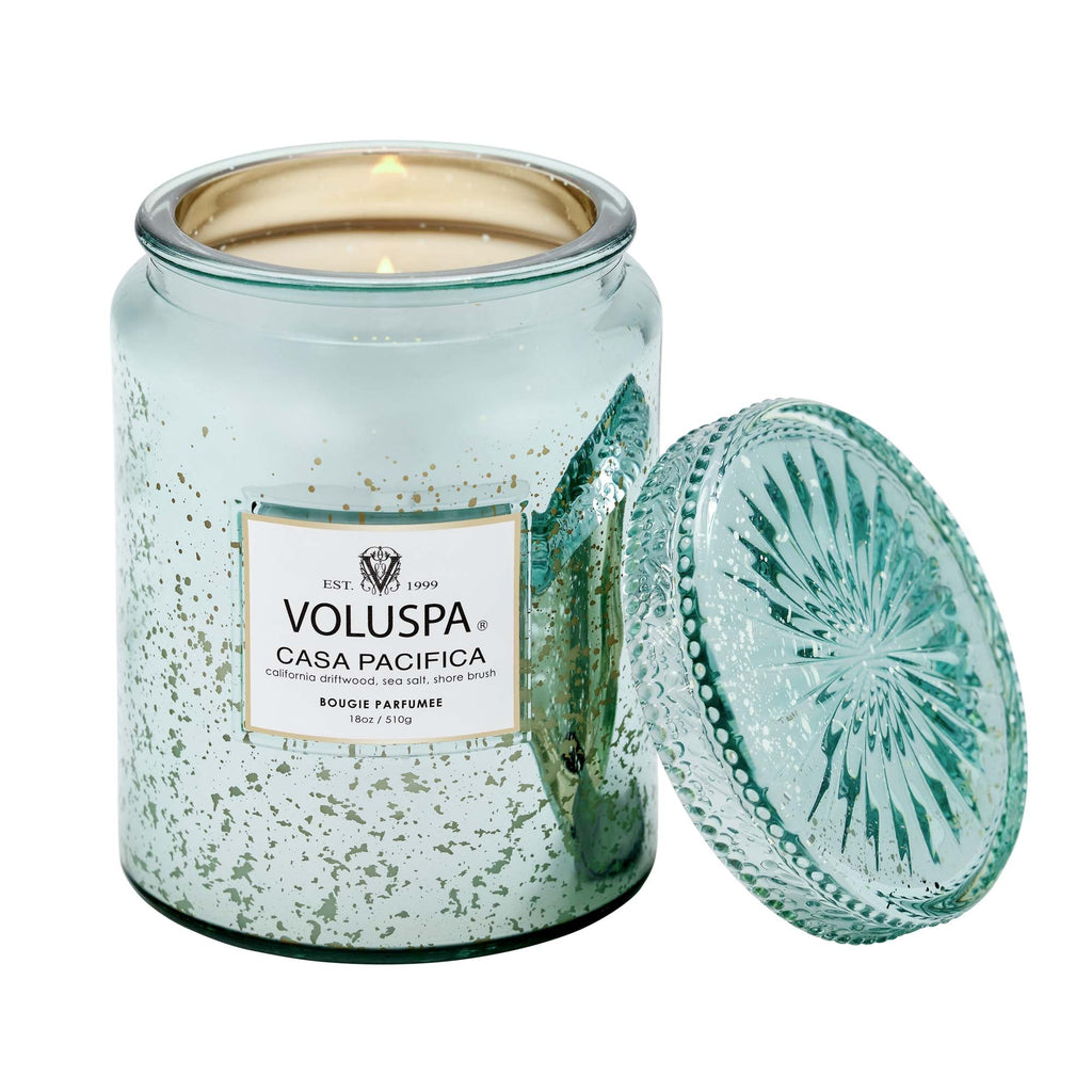 The Voluspa Casa Pacifica Large Jar 18oz Candle features a light turquoise and gold design. Its coconut wax blend offers subtle hints of California driftwood, with the lid set aside for display.