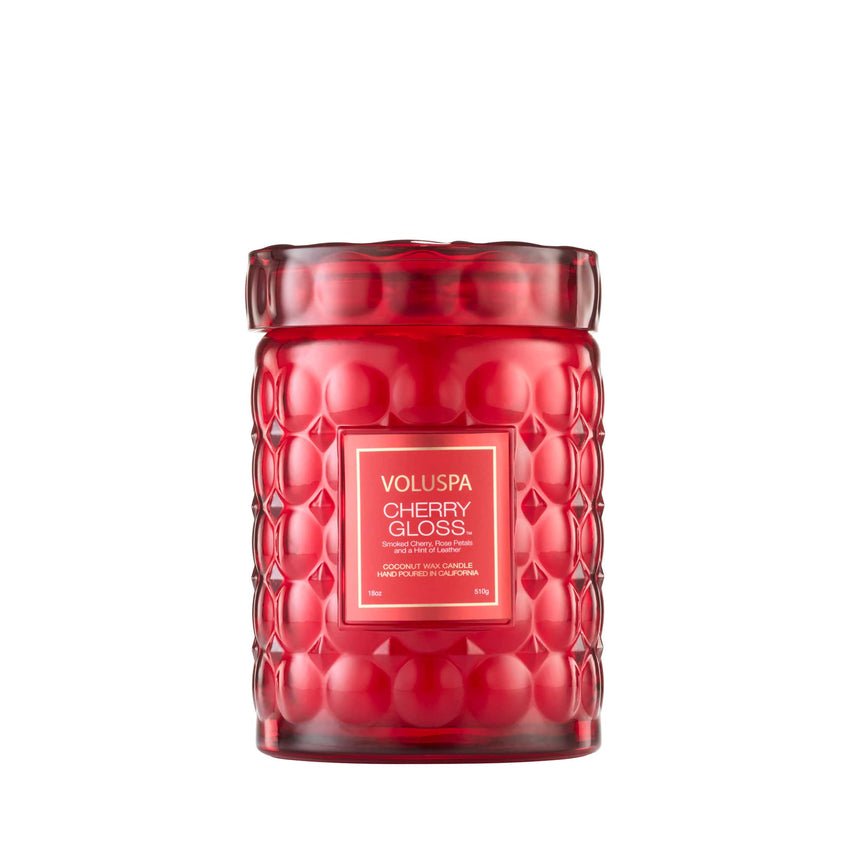 The Voluspa Cherry Gloss Large Jar 18oz Candle features a textured red glass design and wide lid, with scent details on a gold and white label. Made from a coconut wax blend, it offers both aesthetic appeal and fragrance harmony.