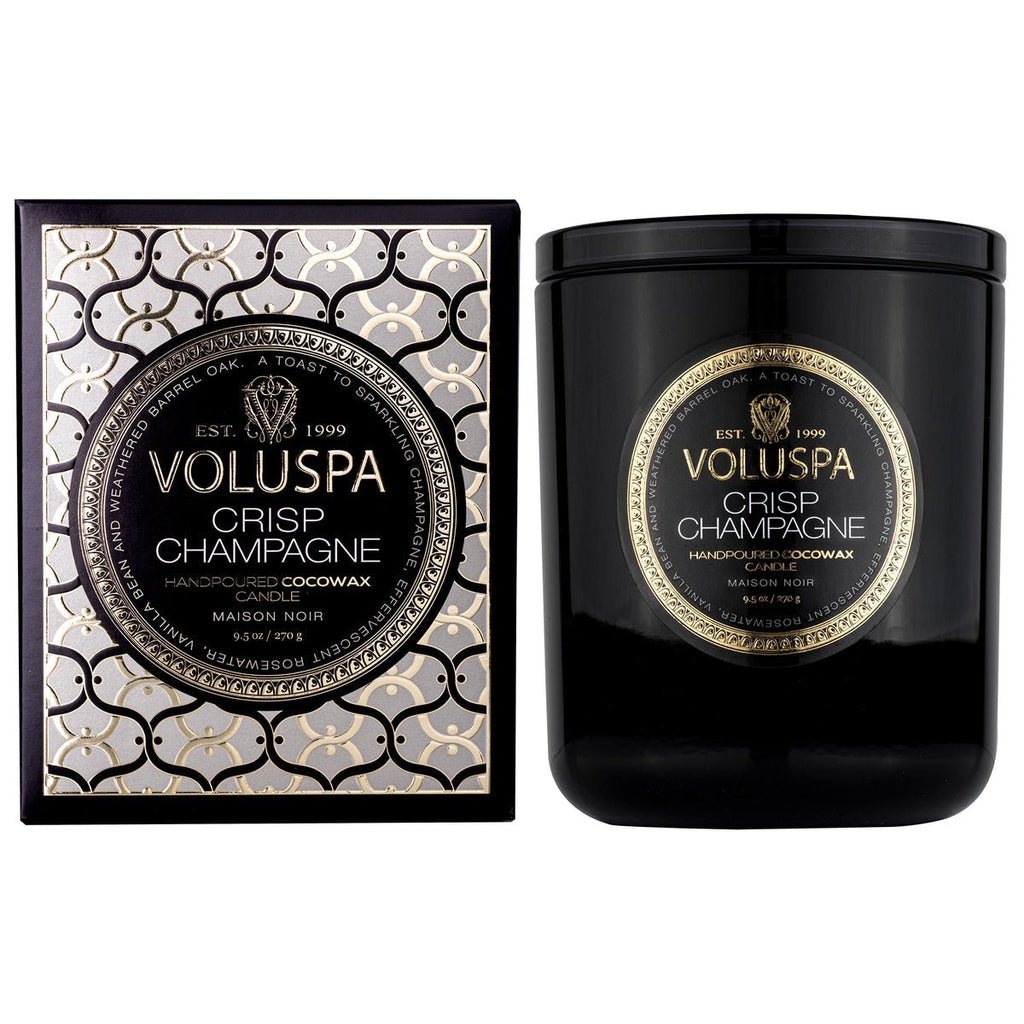 The Voluspa - Crisp Champagne 9.5oz Classic Candle comes in an embossed glass vessel with gold and white details. This sleek, glossy container is made from a coconut wax blend, featuring ornate circular designs and the Crisp Champagne label.