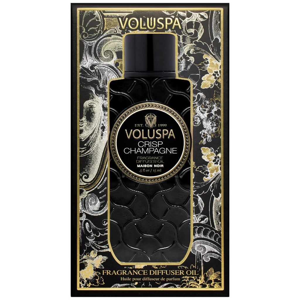 The Voluspa - Crisp Champagne Ultrasonic Diffuser Oil is elegantly packaged in black and gold, showcasing ornate floral designs. The cylindrical bottle features a beautifully patterned surface, complementing the luxurious scent experience by Voluspa.