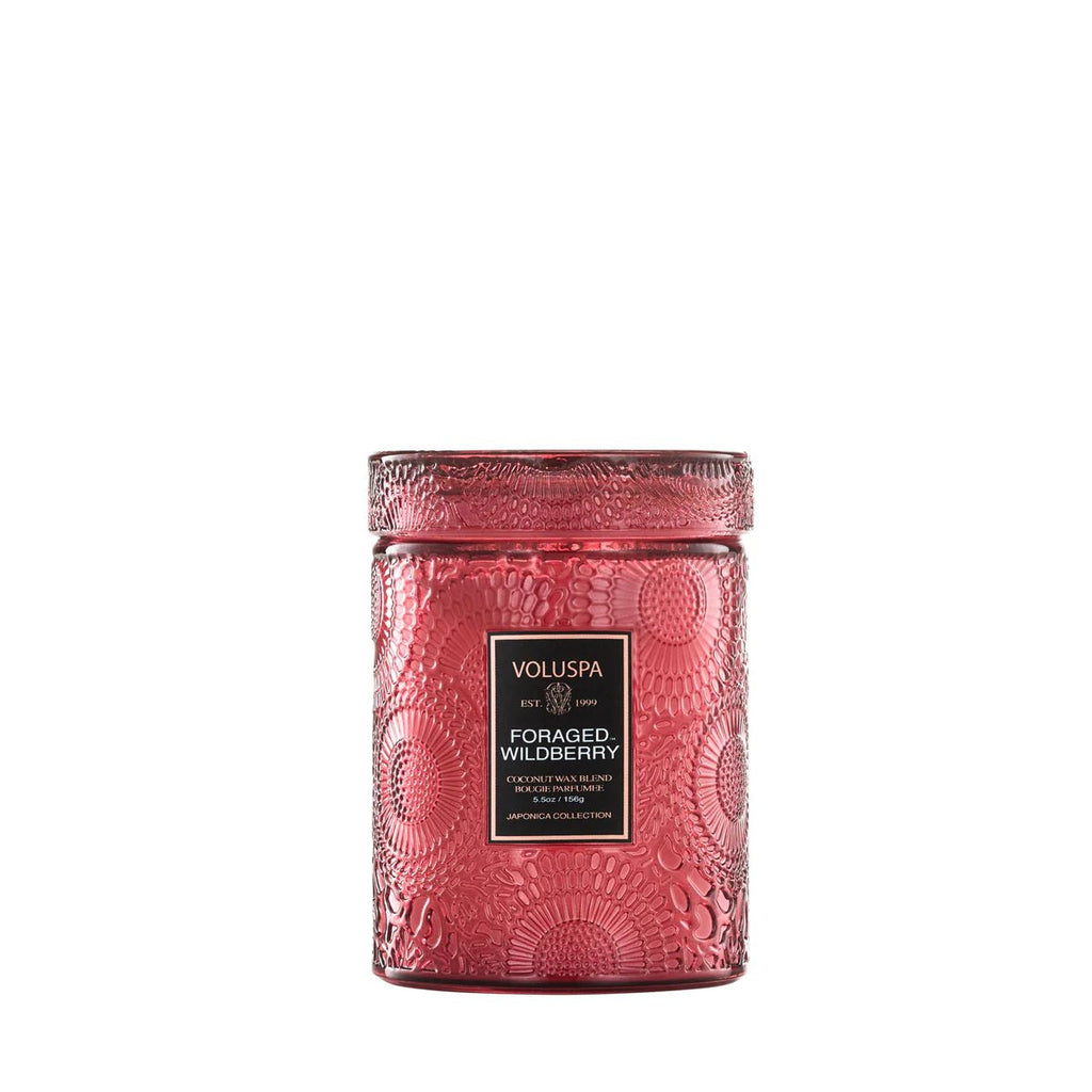 The Voluspa Foraged Wildberry Small Jar 5.5oz Candle features a textured red glass jar with a matching lid and a black-and-gold label, offering the rich scent of wildberry in every burn against a sleek white background.