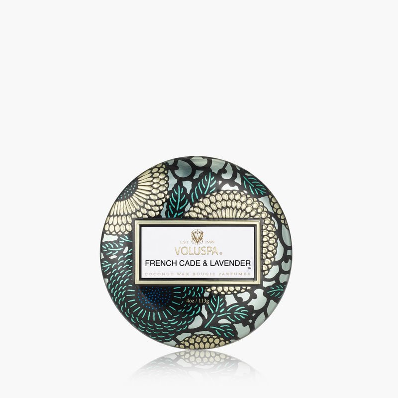 The Voluspa - French Cade Lavender Tin 4oz Candle features decorative gold, teal, and black floral patterns. This mini coconut wax candle delivers notes of French cade wood and lavender, beautifully presented in a round tin.