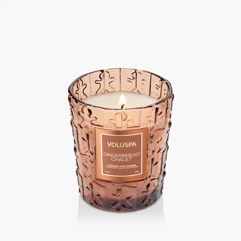 The Voluspa - Gingerbread Chalet Classic 6.5oz Candle comes in a textured brown glass jar with gingerbread designs and a festive label, adding cozy holiday charm with its coconut wax gingerbread scent.