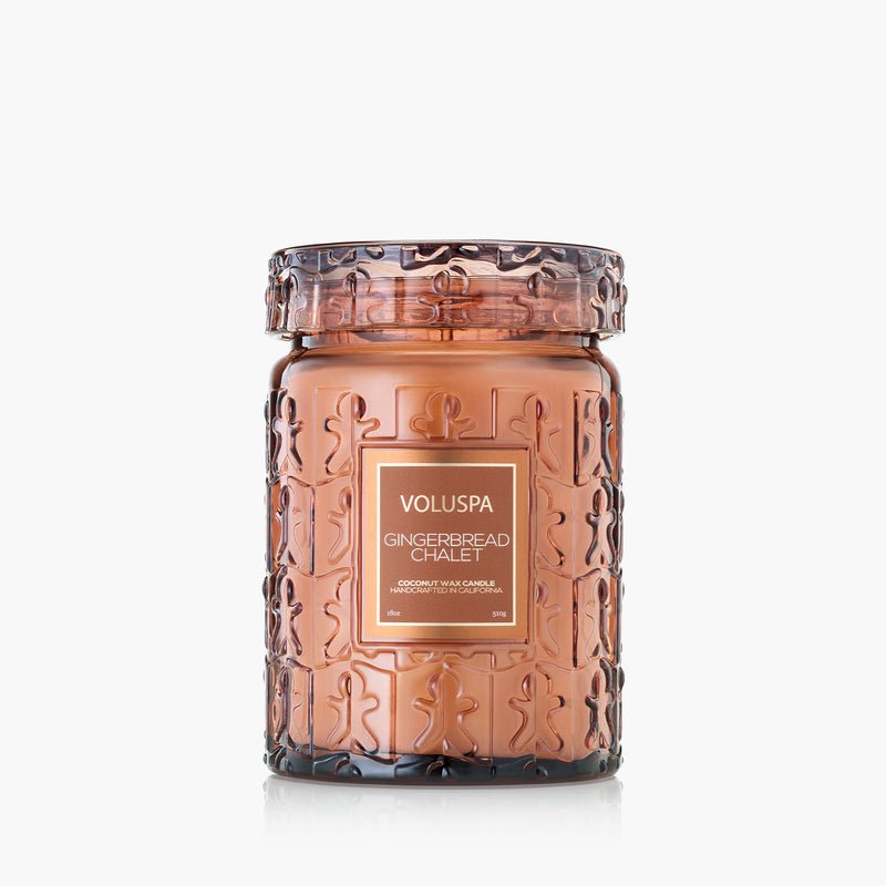 The Voluspa Gingerbread Chalet Large Jar 18oz Candle features an amber glass jar with a festive gingerbread man design and a holiday fragrance, made with a coconut wax blend, and is shown against a plain white background.