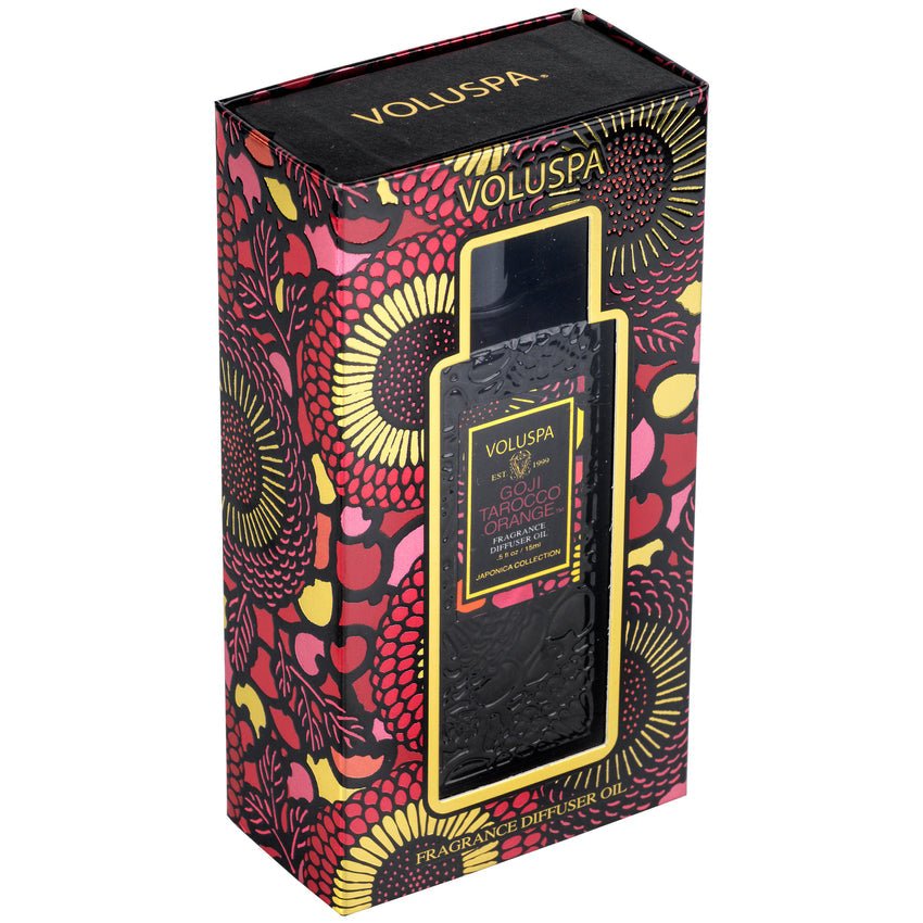 The Voluspa - Goji Torocco Orange Ultrasonic Diffuser Fragrance Oil, elegantly packaged by Voluspa, features vibrant floral patterns in red, yellow, and black. A transparent window reveals the citrus-scented bottle inside—a blend of fragrance artistry.