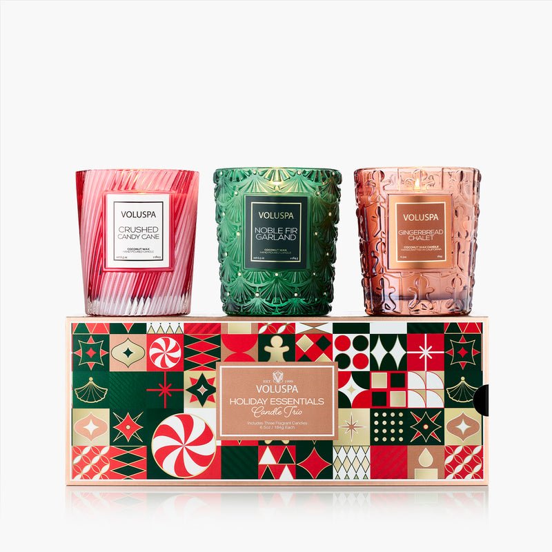 The Voluspa Holiday Essentials Candle Trio Gift Set includes three classic candles in red, green, and rose gold glass, featuring Crushed Candy Cane, Noble Fir Garland, and Gingerbread Vanilla scents in a festive holiday box.