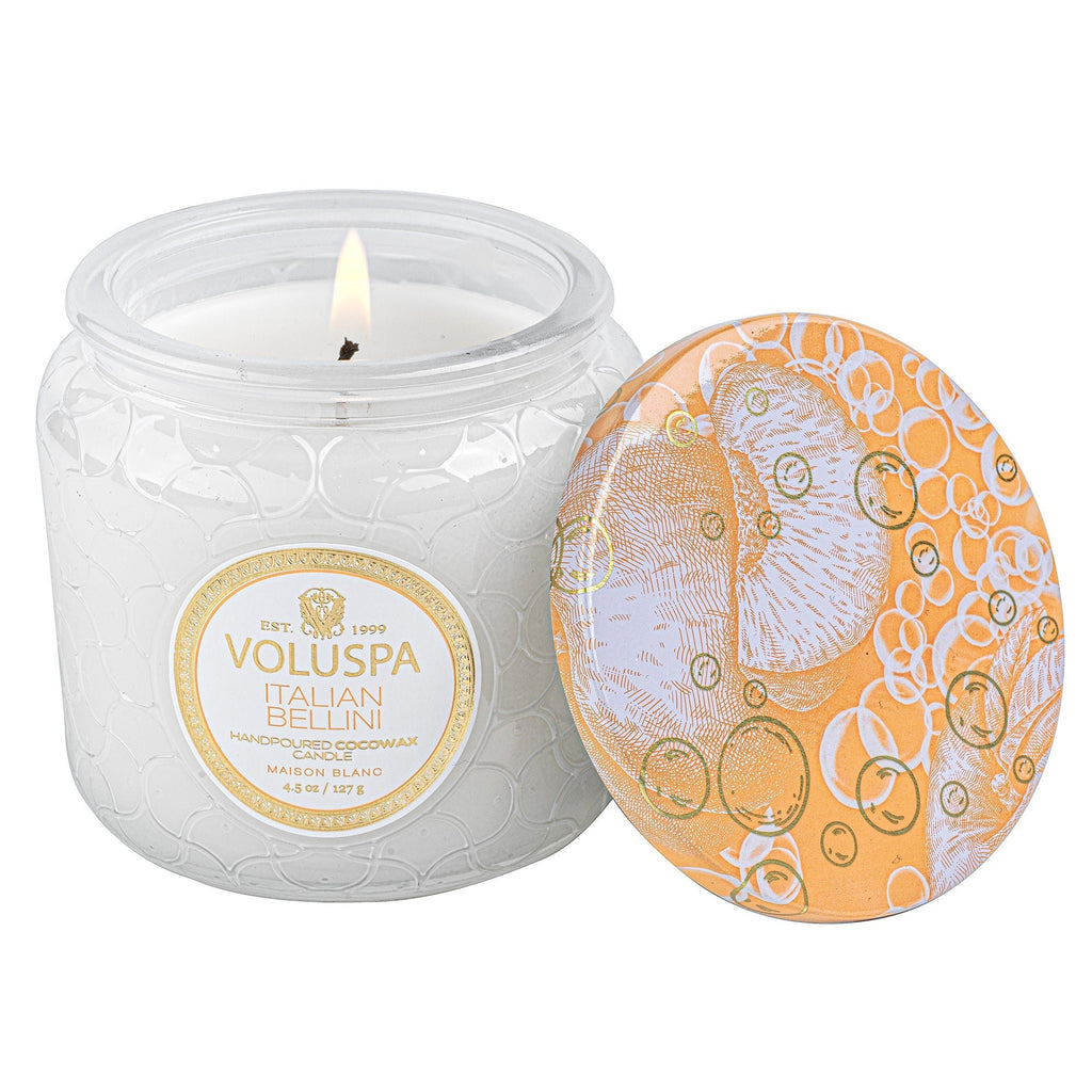 The Voluspa Italian Bellini Petite Jar Candle (4.5oz) in a textured glass jar emits a refreshing citrus fragrance. The orange lid, adorned with an intricate white and gold bubble pattern, perfectly complements the coconut wax blend inside.