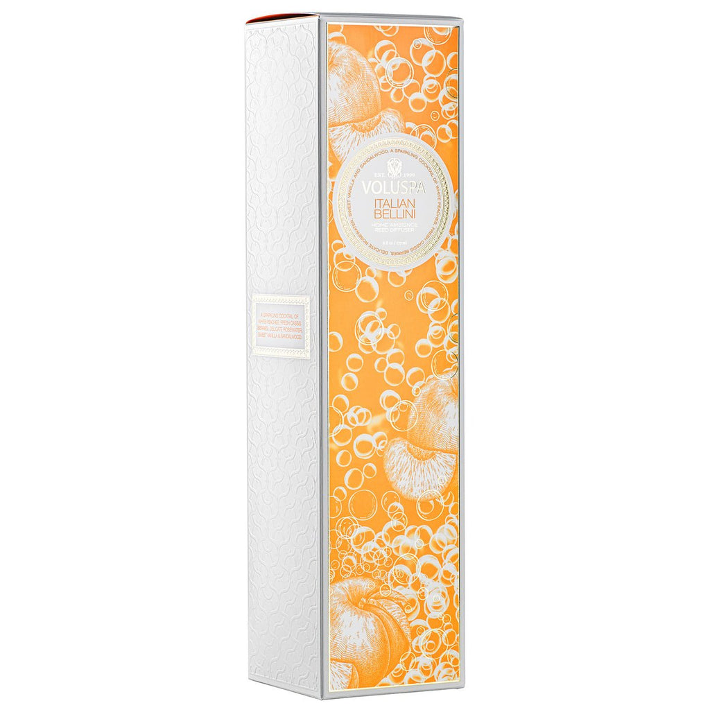 The tall box has a white and orange design with circular patterns and fruit illustrations, evoking sparkling champagne. It reads Voluspa Italian Bellini and features a subtle embossed pattern, ideal for the Voluspa - Italian Bellini Reed Diffuser.