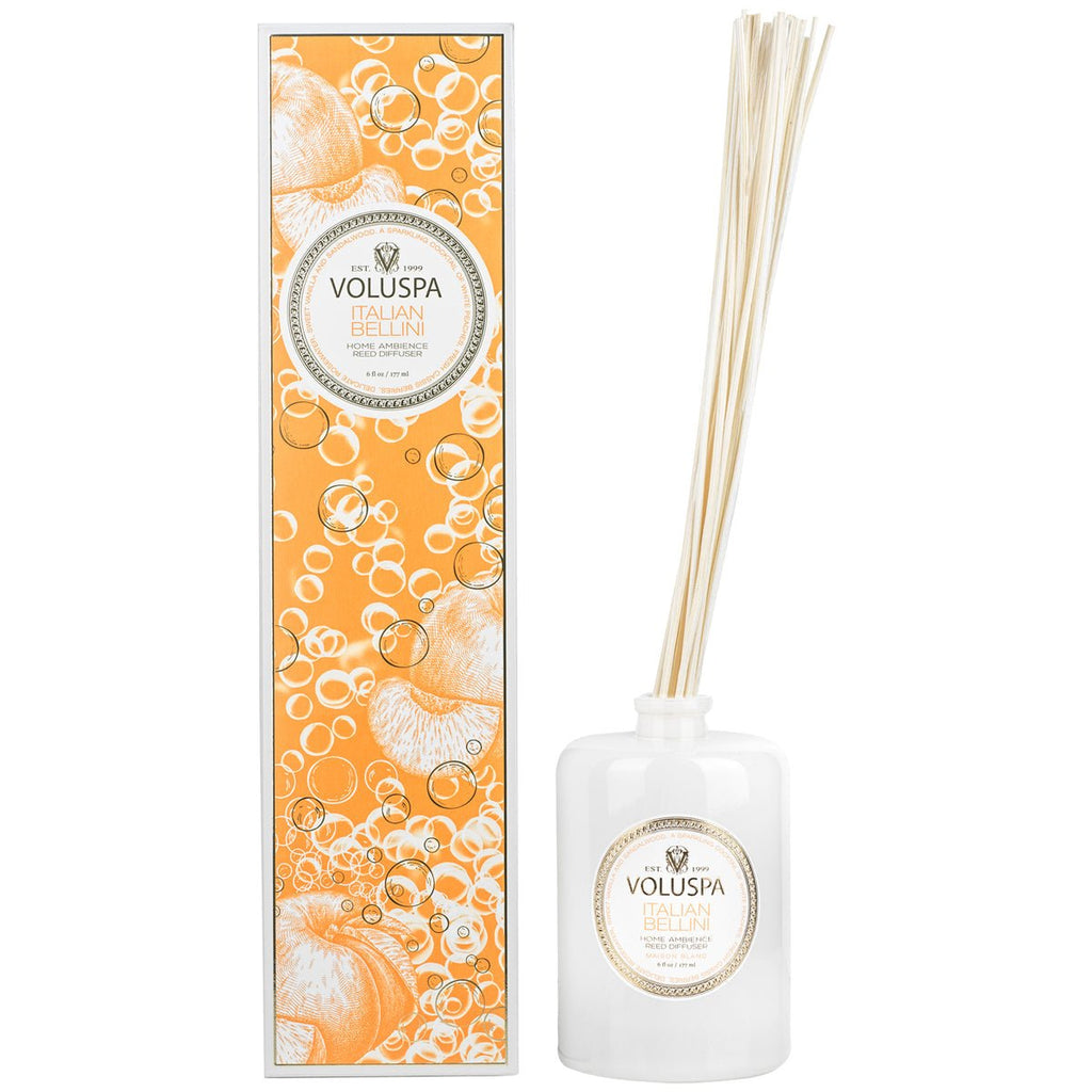 The Voluspa Italian Bellini Reed Diffuser set includes a white bottle with reeds and a decorative box. The orange and white box, adorned with bubble and fruit illustrations, captures the essence of sparkling champagne and juicy white peach fragrance oil.