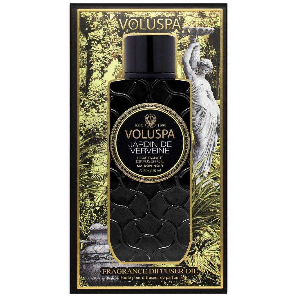 The image showcases a Voluspa - Jardin De Verveine Blanc Ultrasonic Diffuser Fragrance Oil package. It features a black bottle with an intricate pattern, enhanced by decorative greenery, verbena, and lemongrass scents, elegantly set against a classical statue design in the background.