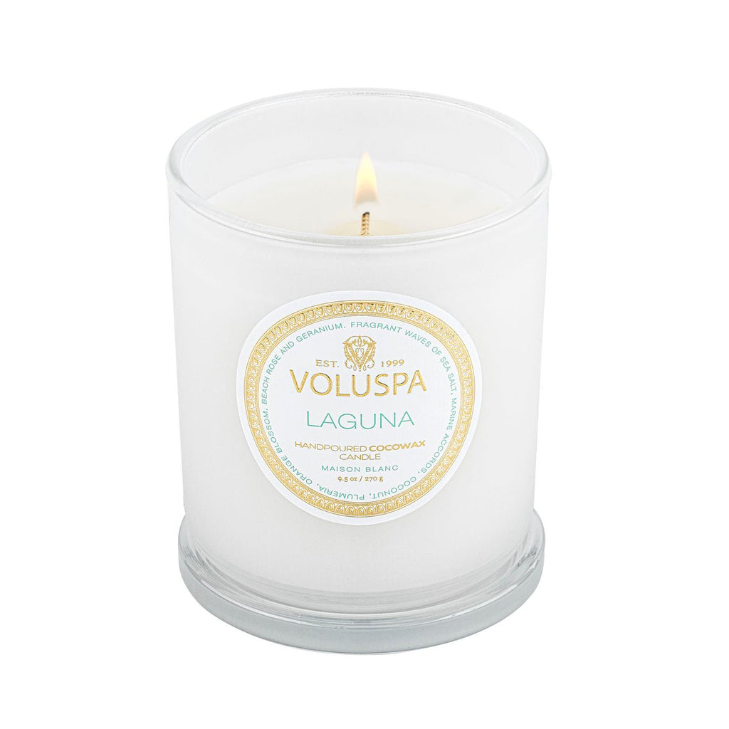 A lit Voluspa - Laguna Classic Candle 9.5oz in a Petite Jar displays elegant lettering. This hand-poured coconut wax blend features a single wick, providing an exquisite fragrance throw as it sits gracefully on a flat surface.