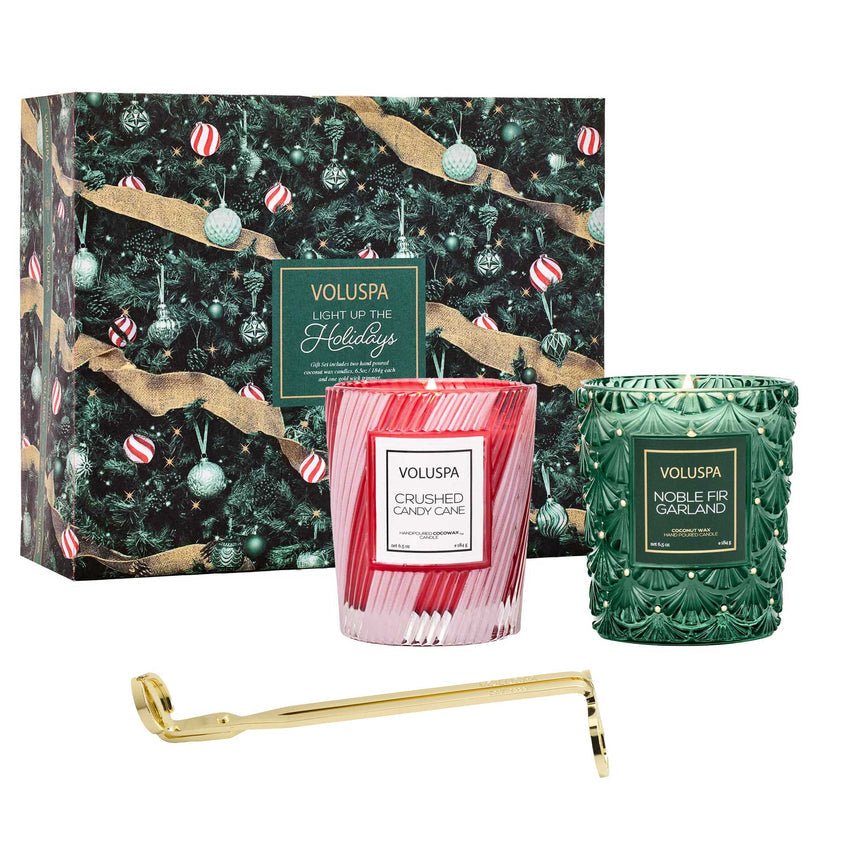 The Voluspa Light Up The Holidays Candle Gift Set features Crushed Candy Cane and Noble Fir Garland candles in a festive box with ornaments, plus a gold wick trimmer for elegance.