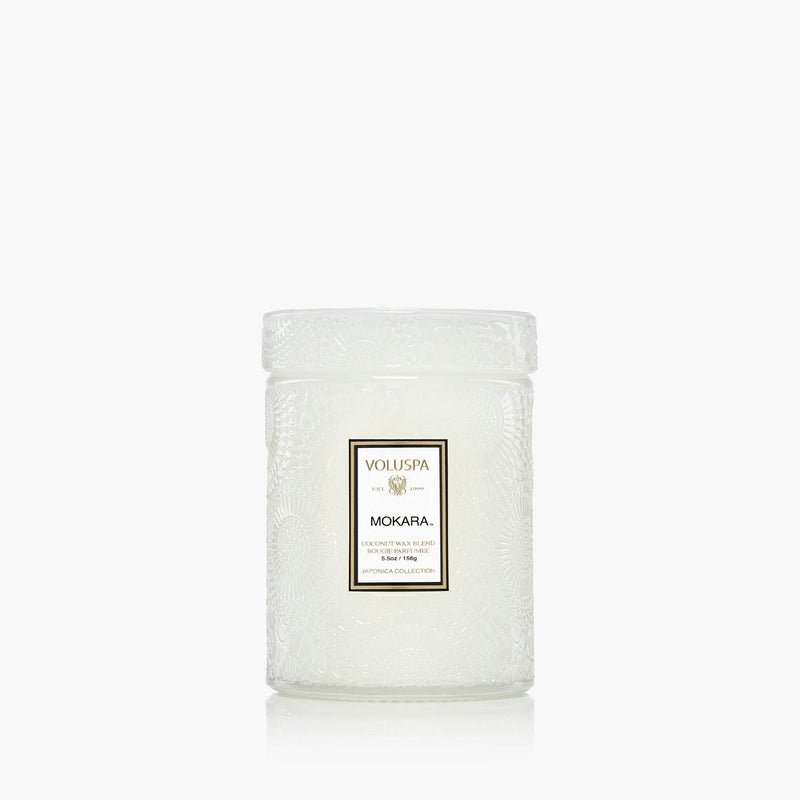 The Voluspa Mokara Orchid 5.5oz Small Jar Candle is a white, embossed glass candle with a lid and gold-black accented label, crafted with a coconut wax blend for a refined floral scent. Background: plain white.