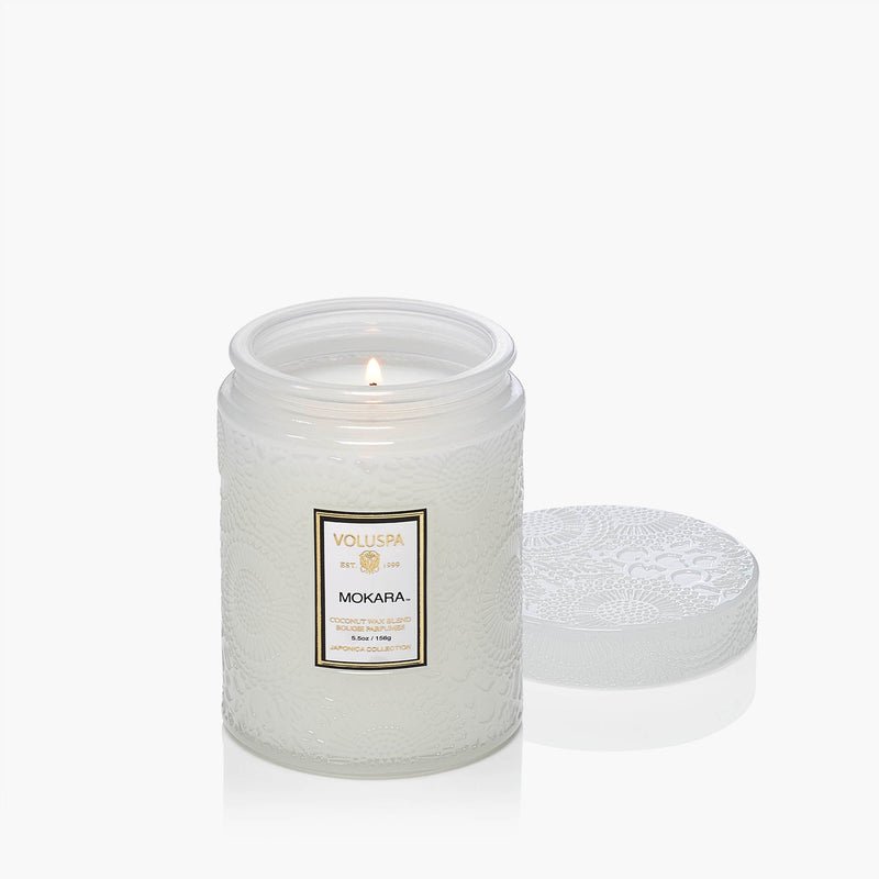 The Voluspa Mokara Orchid 5.5oz Small Jar Candle, crafted from a coconut wax blend, burns in an embossed glass jar with a matching lid beside it—all set against a plain white background.