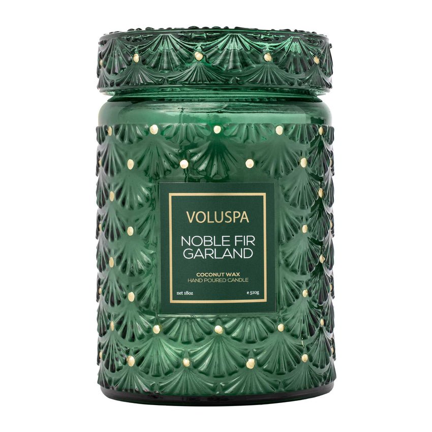 The Voluspa - Noble Fir Garland Large Jar 18oz Candle features a green jar with a fir tree pattern, woody fragrance, and a label stating its coconut wax and hand-poured creation.