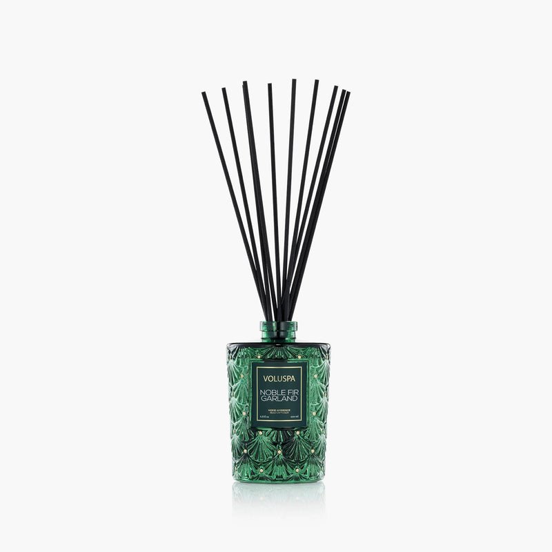 A green Voluspa - Noble Fir Garland Reed Diffuser with black reeds, filled with Noble Fir and cedarwood oil, displayed against a plain white background.