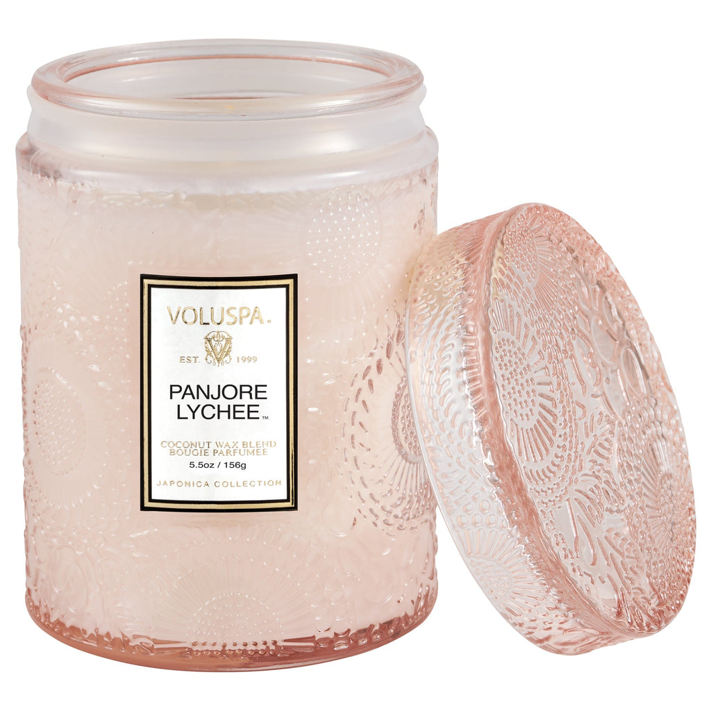 The Voluspa Panjore Lychee vegan candle features a pink textured glass jar with floral etchings and an open lid. The label reads Voluspa - Coconut Wax Blend - 5.5 oz/156 g - Japonica Collection, exuding elegance and style.