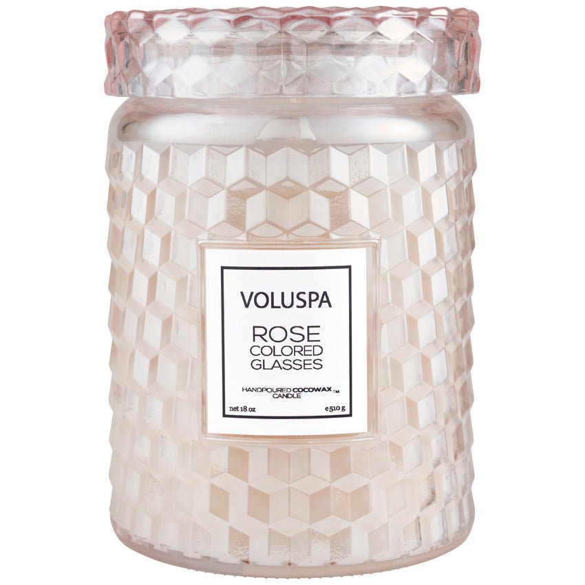 The Voluspa - Rose Colored Glasses Large 18oz Jar Candle, tinted soft pink with a decorative lid, is hand-poured with coconut wax and fills spaces with a delicate floral fragrance.