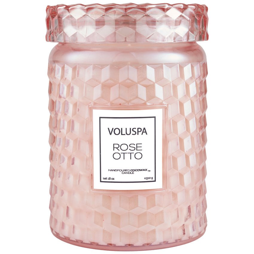 The Voluspa - Rose Otto Large 18oz Jar Candle comes in a pink textured glass jar with a geometric design and lid. It features a light pink coconut wax blend, offering an alluring floral fragrance.