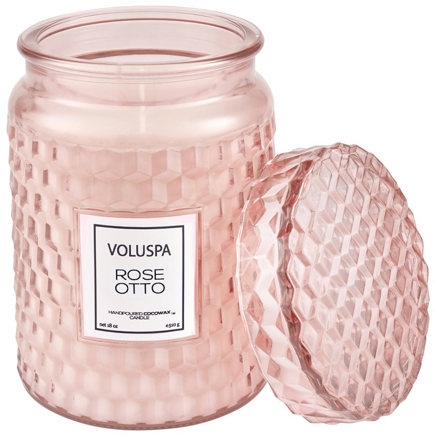 The Voluspa Rose Otto Large 18oz Jar Candle features a textured, partially transparent pink glass jar with an intricate geometric pattern. It has an open lid and a coconut wax blend that releases a delightful floral fragrance.