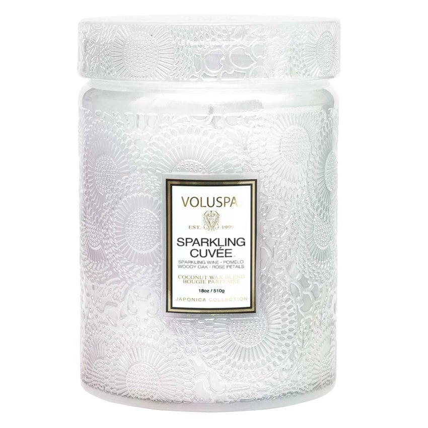 The Voluspa Sparkling Cuvée Large Jar 18oz Candle features a translucent, textured glass with intricate floral patterns, a white Voluspa Sparkling Cuvée label, and a coconut wax blend from the Japonica Collection, delivering an enchanting fragrance.