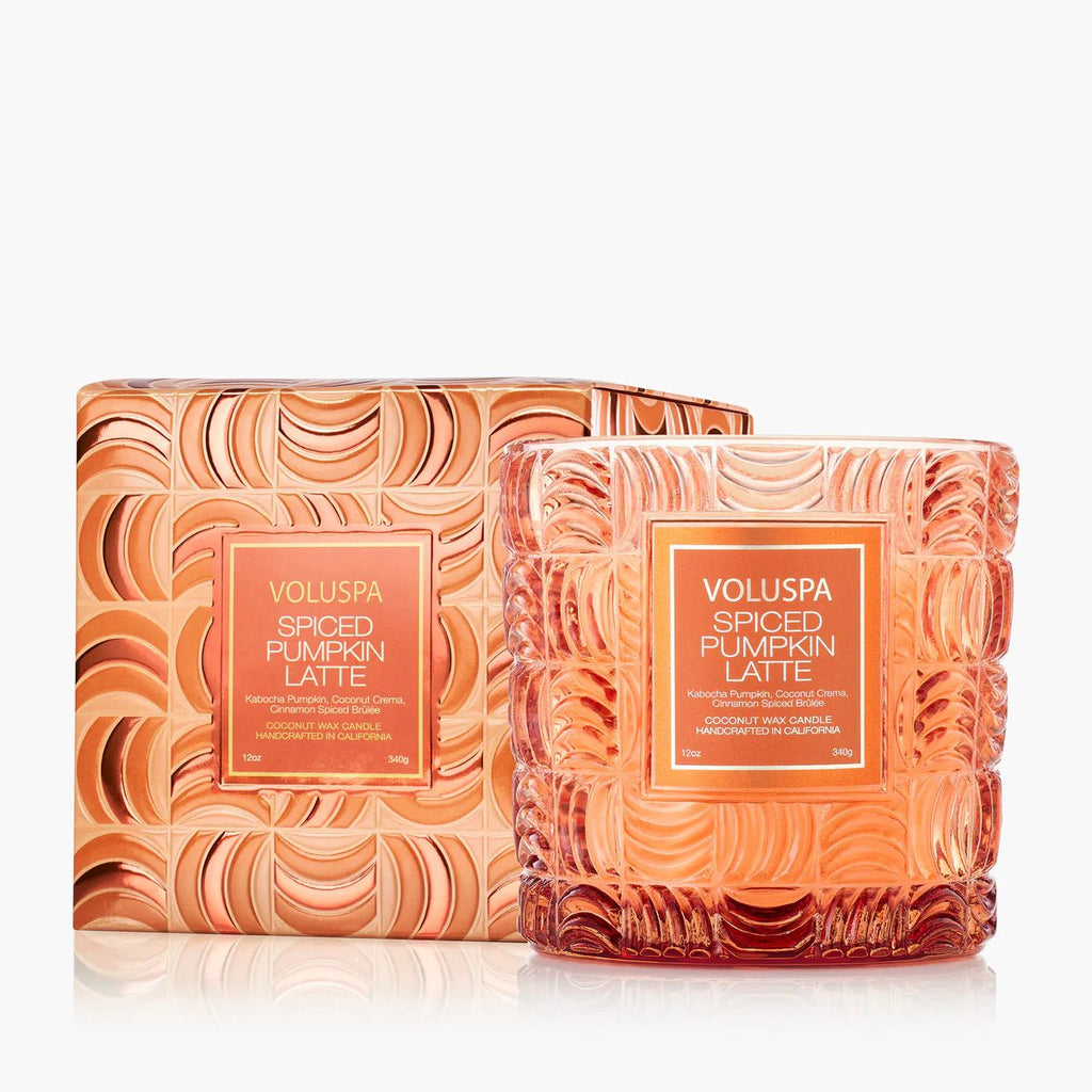 The Voluspa - Spiced Pumpkin Latte Classic 12oz Candle features a coconut wax blend and comes in a matching orange and gold geometric-patterned box, creating a luxurious, autumn-inspired look.