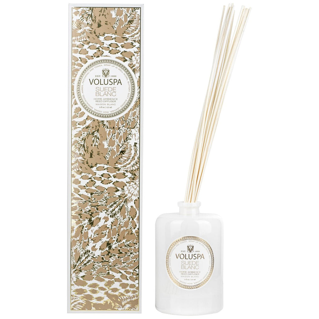 The Voluspa - Suede Blanc 172ml Reed Diffuser comes in a stylish gold and white box, featuring a white glass bottle with fragrance oil and thin reeds that diffuse a buttery sueded leather scent without needing a flame.