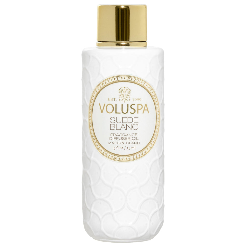 The Voluspa - Suede Blanc Ultrasonic Diffuser Oil comes in a textured white bottle with a gold cap and a central label featuring the brand and scent name in elegant gold and black text, offering sueded leather sophistication.