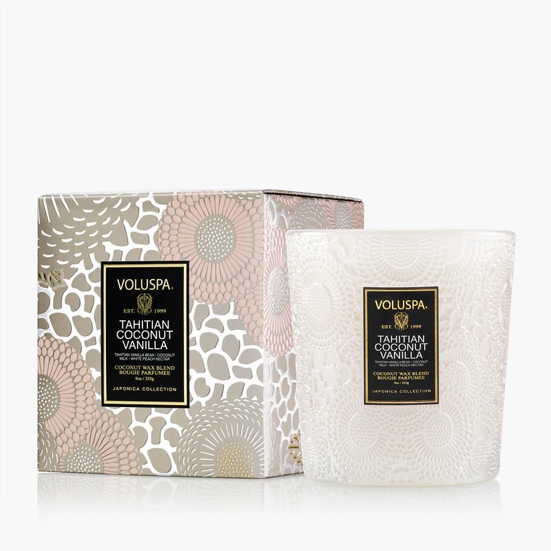 The Voluspa Tahitian Coconut Vanilla Classic 9oz Candle comes in a decorative white glass jar with black and gold labels, accompanied by a matching patterned box featuring elegant floral designs.