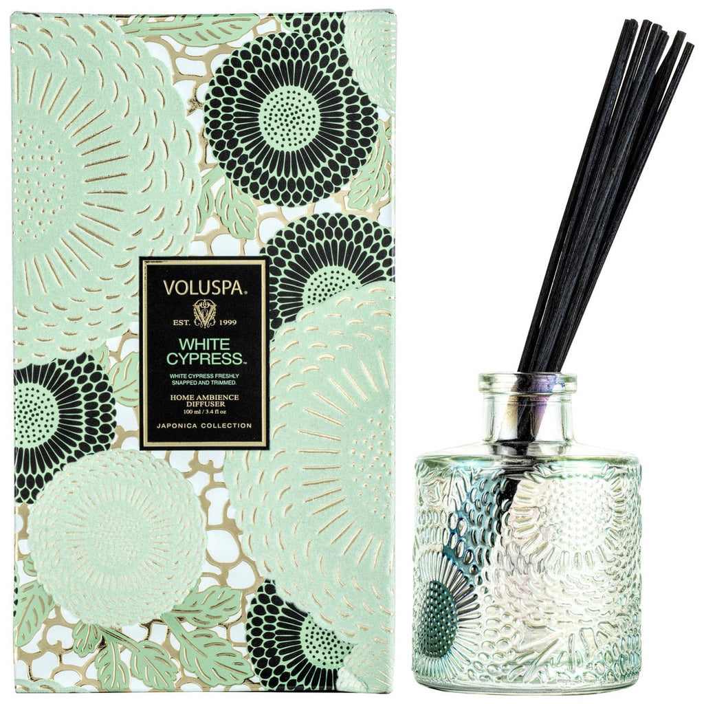 Discover the Voluspa - White Cypress Reed Diffuser from the Japonica Collection, featuring a beautifully patterned mint green and black box. It includes a textured glass jar with Evergreen Wood-scented oil and black reeds for an aromatic experience.