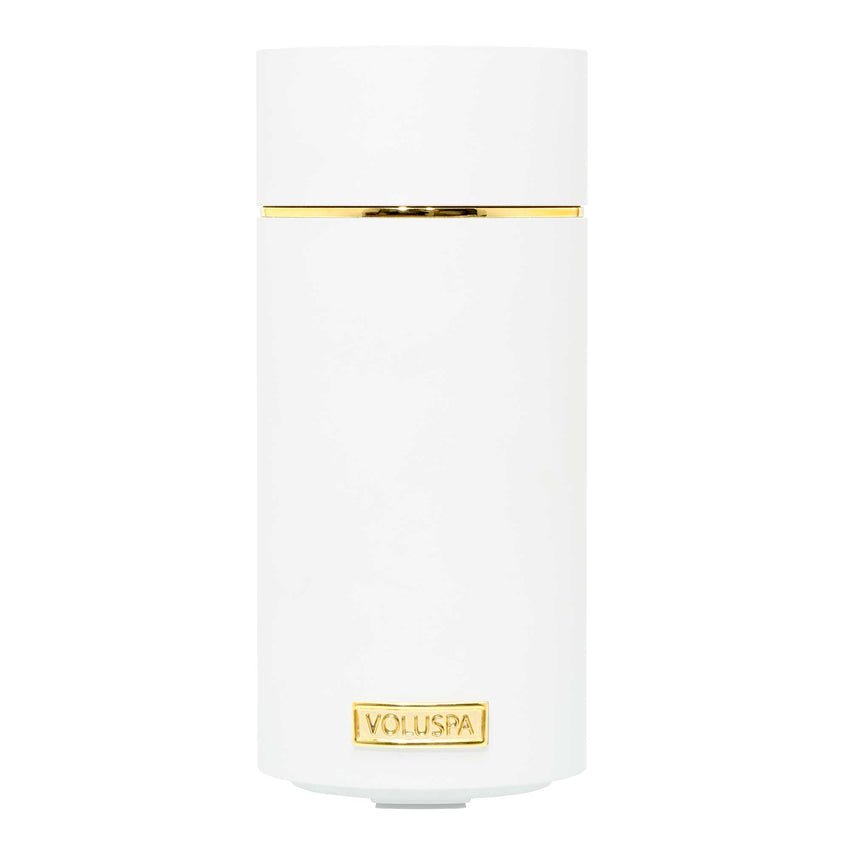 A sleek, white cylindrical cordless diffuser with a minimalistic design features a gold accent and a rectangular gold label near the base embossed with Voluspa is called the Voluspa - White Ultrasonic Fragrance Oil Diffuser Device.