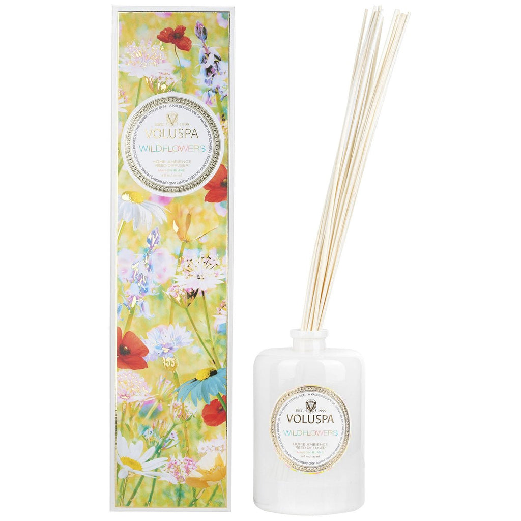 A white diffuser bottle with reeds, labeled Voluspa - Wildflowers 172ml Reed Diffuser, stands beside a tall, colorful box adorned with floral illustrations.